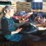 Annette Lachmann sitzt zwischen Instrumenten und spielt Handpan